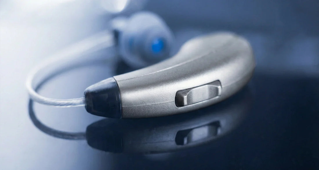 Close-up of a silver hearing aid on a reflective surface with a blurred background