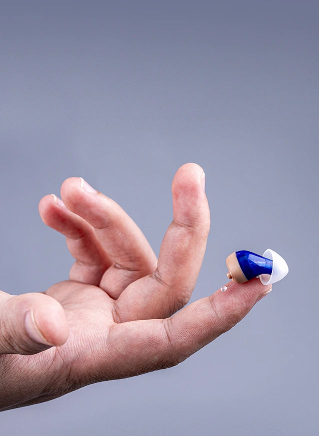 The tiny Tomore CIC hearing aid rests on the fingertip.