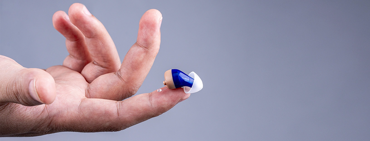 The Tomore 6120 left ear hearing aid rests on the tip of a finger.
