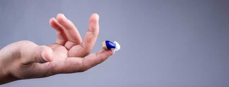 The tiny Tomore CIC hearing aid rests on the fingertip.